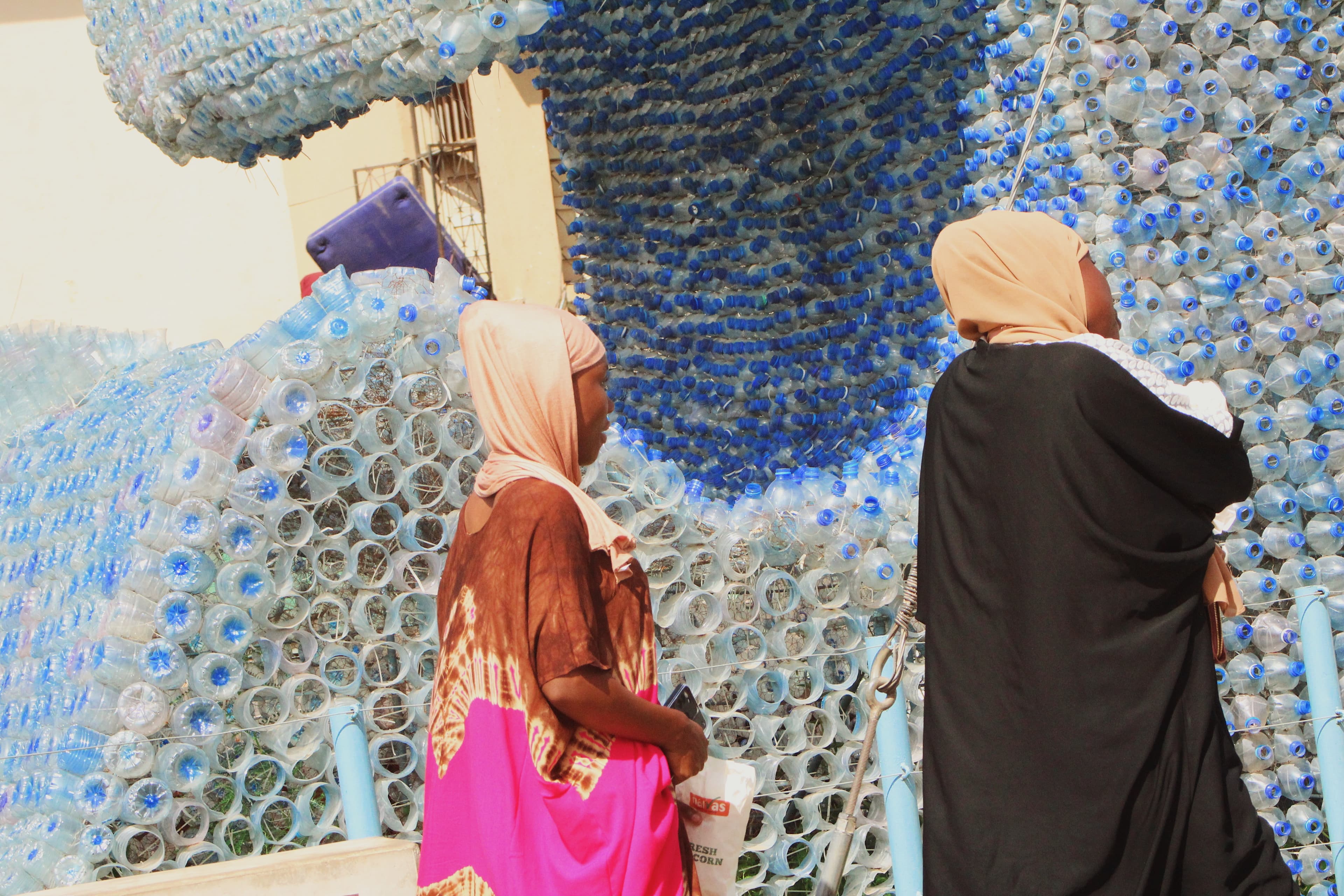 Dos mujeres frente a un muro hecho con botellas de plástico